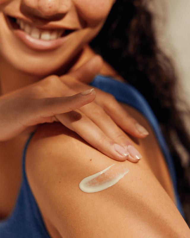 Krupni kadar nanošenja hidratantne Nivea kreme na rame i nadlakticu nasmijane djevojke