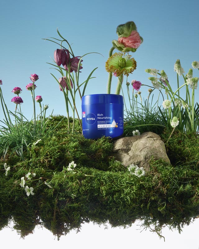 Plava posuda Nivea Rich Nourishing kreme za tijelo okružena mahovinom, stijenom i poljskim cvijećem