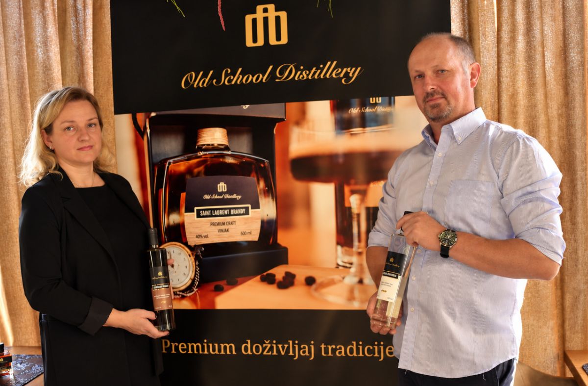 Predstavnici brenda Old School Distillery drže boce svojih alkoholnih pića ispred promotivnog plakata