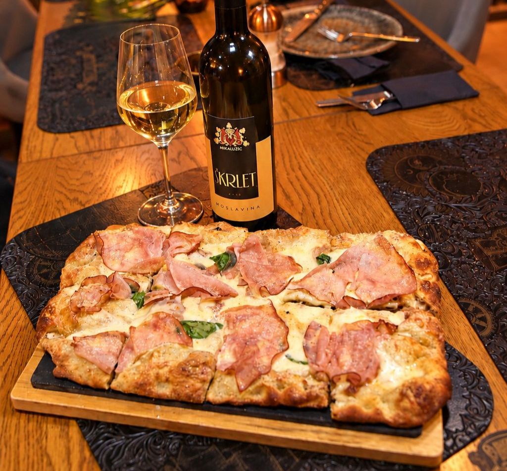 Pala Romana by Domagoj Kralj na drvenoj plati poslužena uz bocu i čašu bijelog vina Miklaužić Škrlet