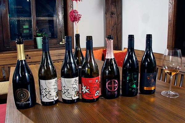 Sedam boca Bolfan vina i čaša s točenim vinom na drvenom stolu