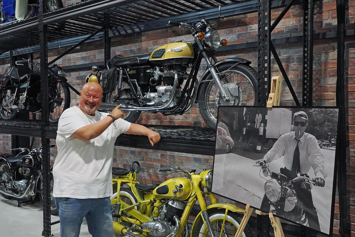 Muškarac u bijeloj majici pokazuje na retro motocikle izložene na policama u muzeju Zlaten Rozhen