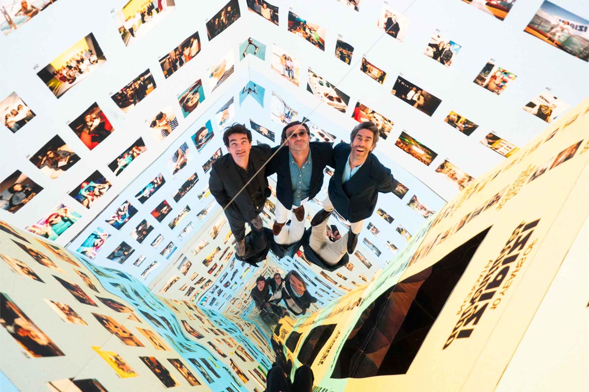 Xavier Aguera, Charles Brun i Quentin Couturier gledaju prema gore unutar zrcalne foto kabine oblijepljene malim fotografijama