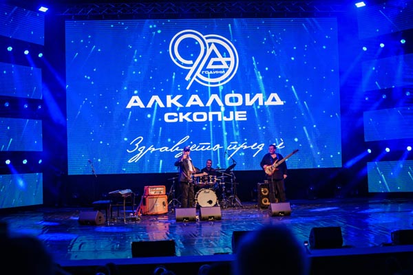 Glazbeni bend na pozornici s logotipom Alkaloid Skoplje za 90 godina u pozadini