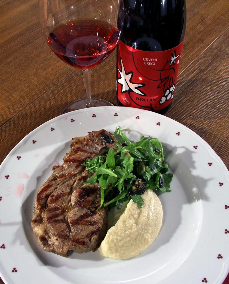 Boca Bolfan Crveni bregi vina, čaša crnog vina i grill odrezak s prilogom na tanjuru