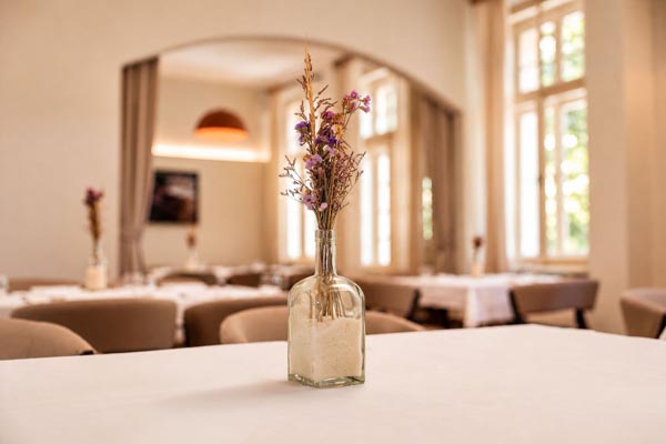 Uređen interijer restorana Bota Šare u Zagrebu s bijelim stolnjacima, bež naslonjačima i vazom sa suhim cvijećem