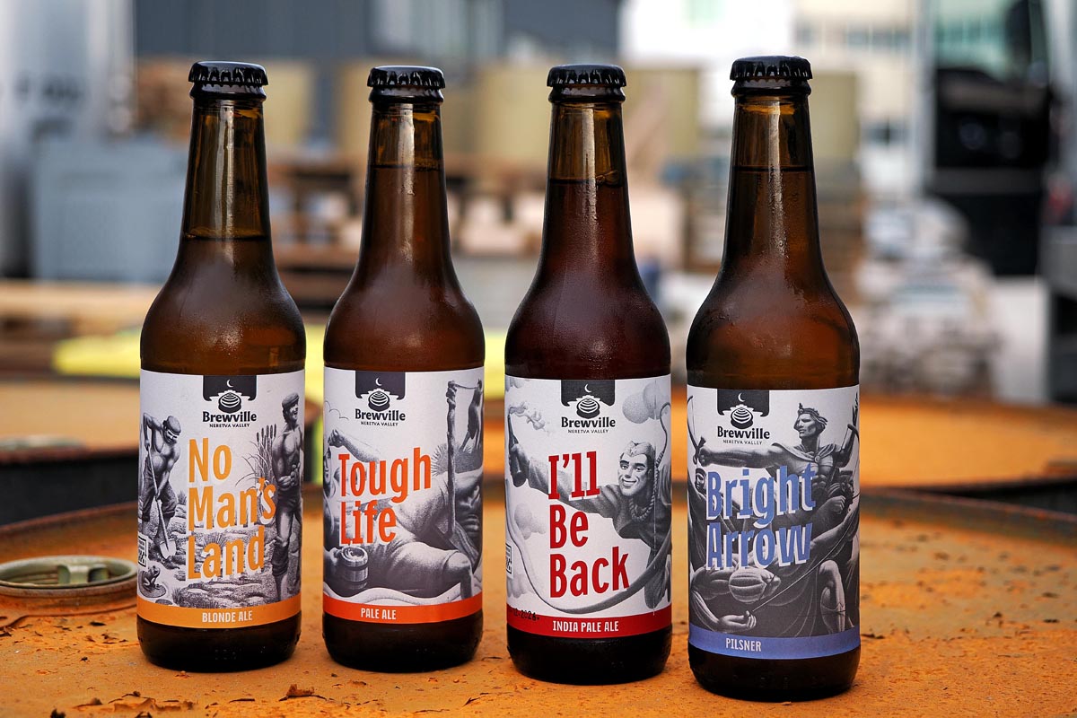 Četiri staklene boce Brewville craft piva s različitim etiketama poredane na hrđavoj površini