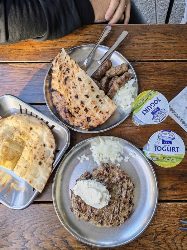 Sarajevski ćevapi i pljeskavica s kajmakom posluženi uz somun, luk i tekući jogurt na drvenom stolu ćevabdžinice Hodžić