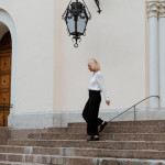 Žena u bijeloj košulji i crnim hlačama silazi niz kamene stube povijesne zgrade kao primjer za poslovni stil