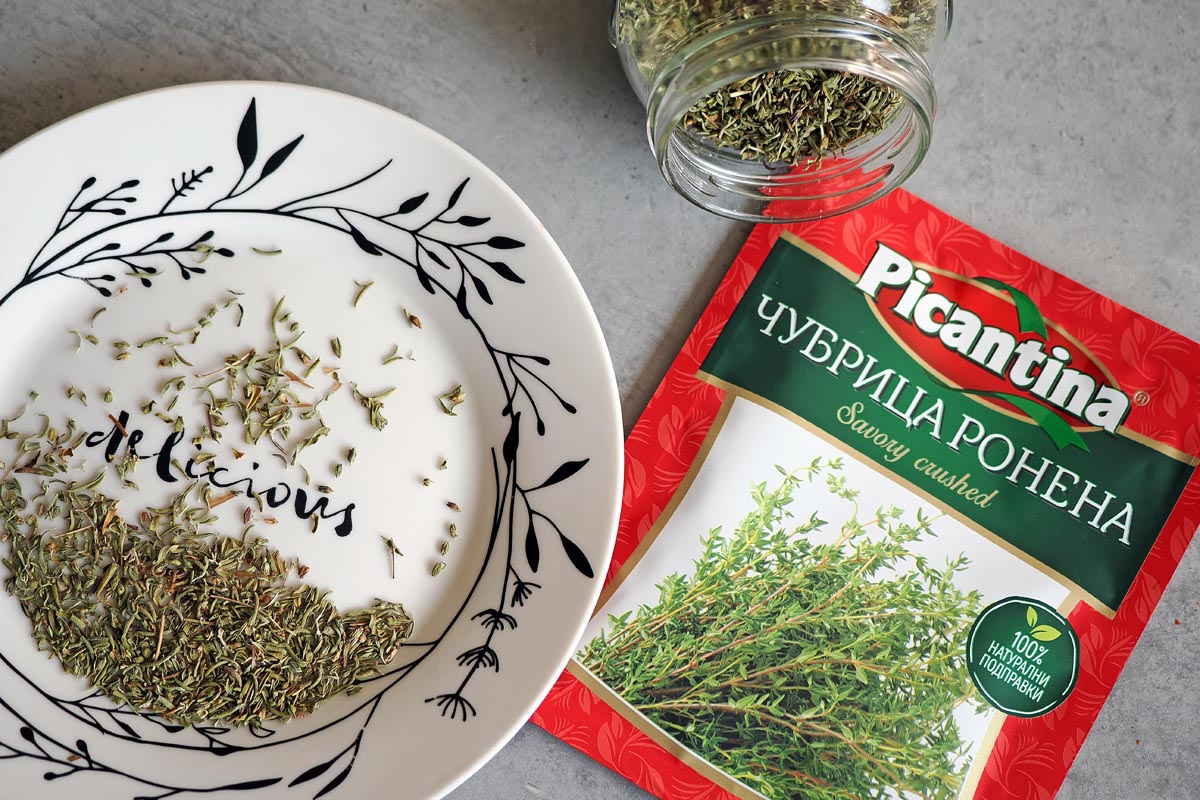 Sušeni začin čubrica posipan po tanjuru s natpisom pored originalnog Picantina pakiranja