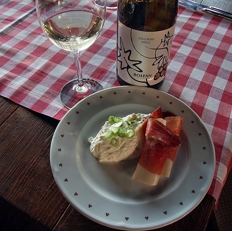 Bolfan vino Zagorski bregi, čaša bijelog vina i predjelo s pršutom na kariranom stolnjaku