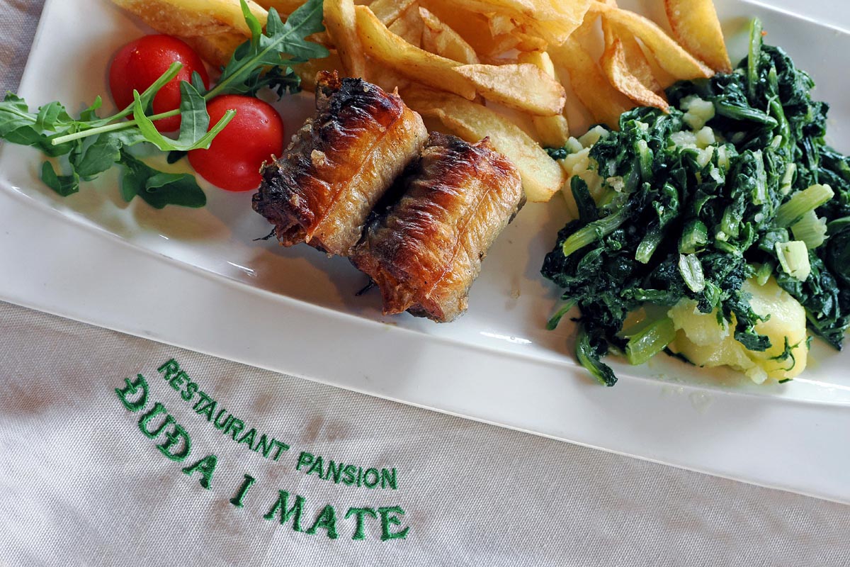 Komadi pečene jegulje s prilogom od blitve, krumpira i cherry rajčica pokraj natpisa Restaurant Đuđa i Mate