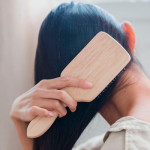 Žena drvenom četkom češlja dugu tamnu kosu gledano s leđa