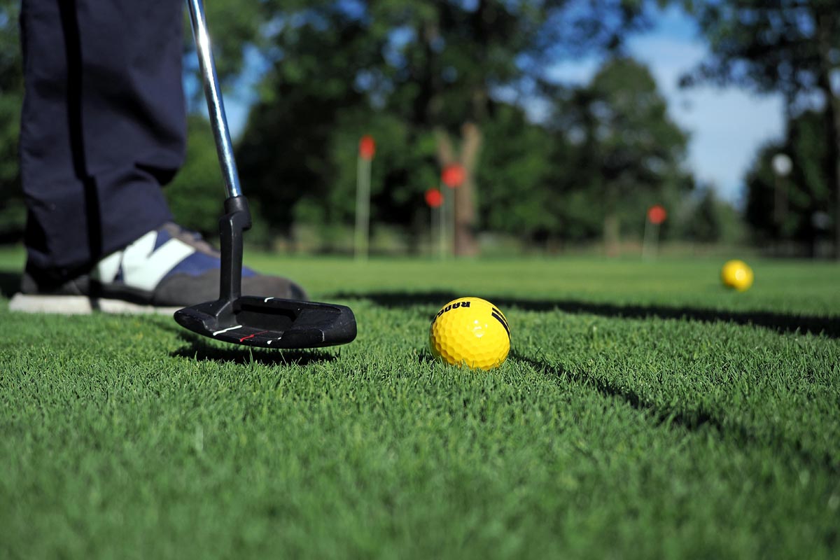 Crna palica tik uz žutu lopticu za golf na šišanoj zelenoj travi