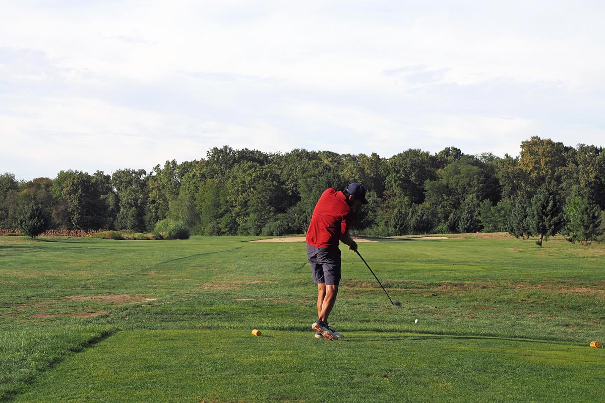 Igrač u crvenoj majici izvodi zamah palicom na prostranom golf terenu Livada okruženom šumom