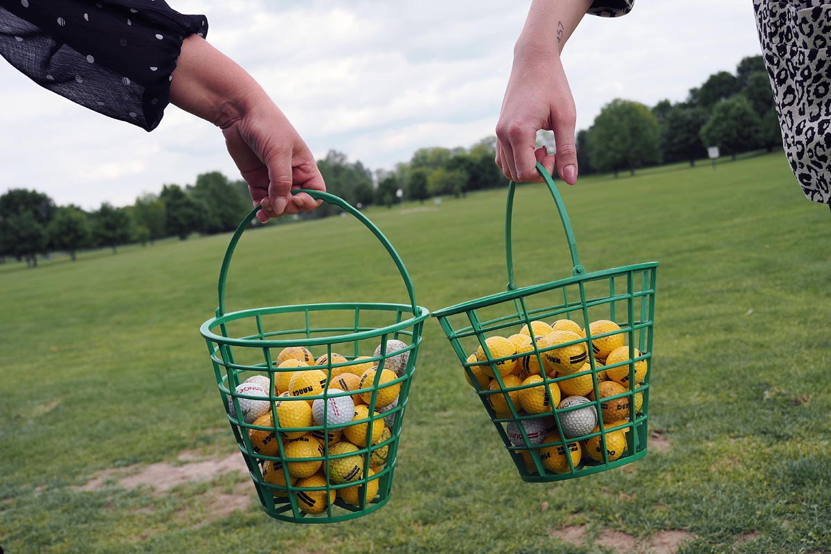 Dvije ženske osobe drže zelene košare prepune žutih i bijelih loptica za golf