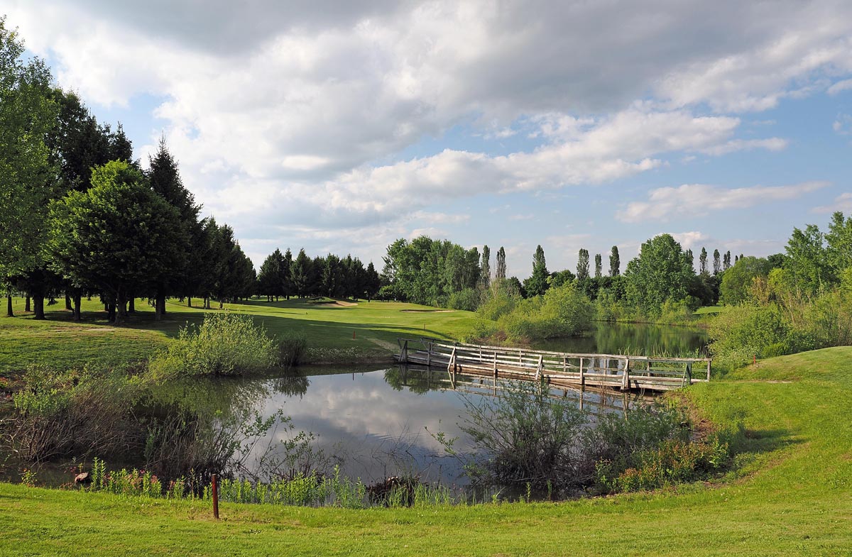 Drveni mostić preko jezerca na zelenom golf terenu Livada pod oblačnim nebom