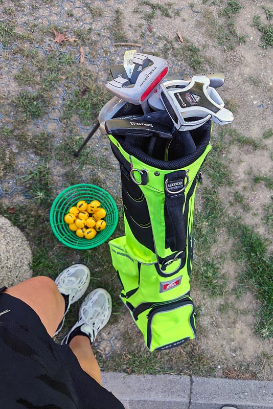 Svijetlozelena torba s palicama za golf i košara sa žutim lopticama na tlu