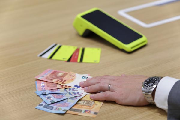 Bankovne kartice i POS uređaj na drvenom stolu uz ruku koja drži euro novčanice