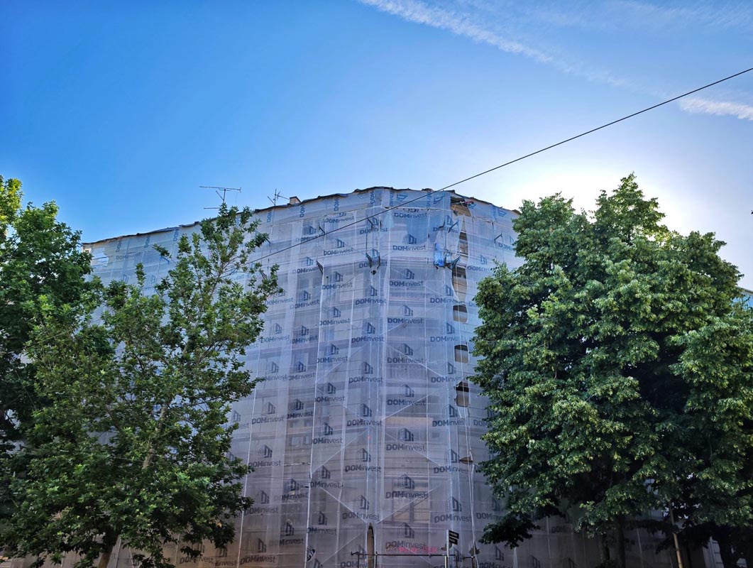 Stambena zgrada u obnovi prekrivena zaštitnom građevinskom skelom i ceradom iza zelenog drveća