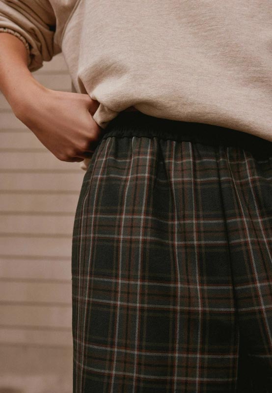Detalj ženskog outfita s tamnim kariranim hlačama i ležernom bež trenirkom s podvrgnutim rukavima