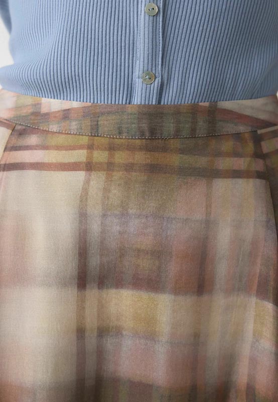 Krupni kadar lagane karirane suknje u pastelnim smeđim i ružičastim tonovima uz plavu pletenu majicu