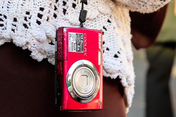 Mali crveni Nikon Coolpix digitalni fotoaparat visi na vezici oko vrata osobe u bijelom pletenom džemperu