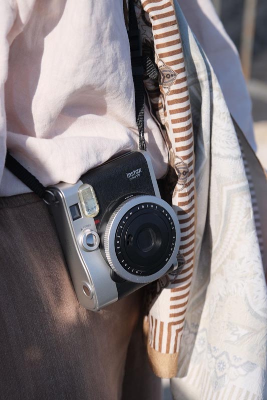 Srebrno-crni Fujifilm Instax Mini 90 fotoaparat na remenu uz ležernu odjeću i prugasti šal