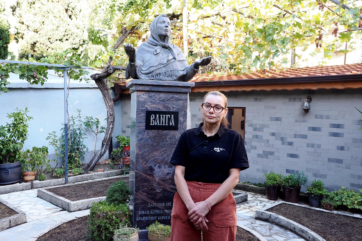 Marija Tamanova stoji pokraj spomenika babi Vangi u dvorištu kućnog muzeja