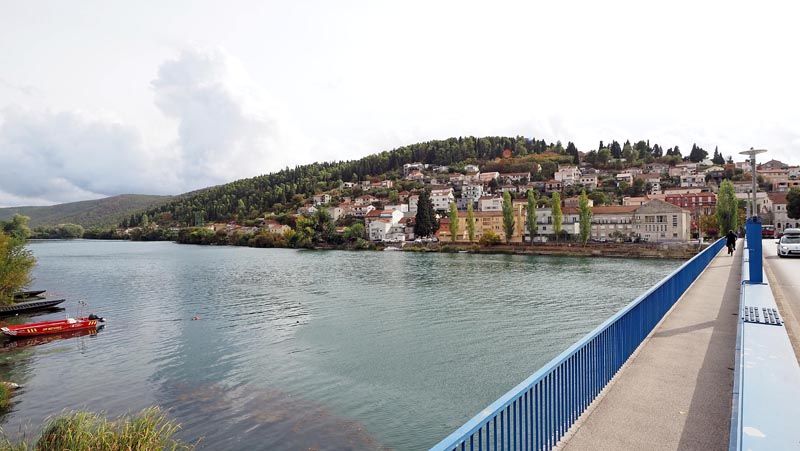 Pogled s lučkog mosta na plavu rijeku Neretvu, crveni čamac i kuće na brežuljku u Metkoviću