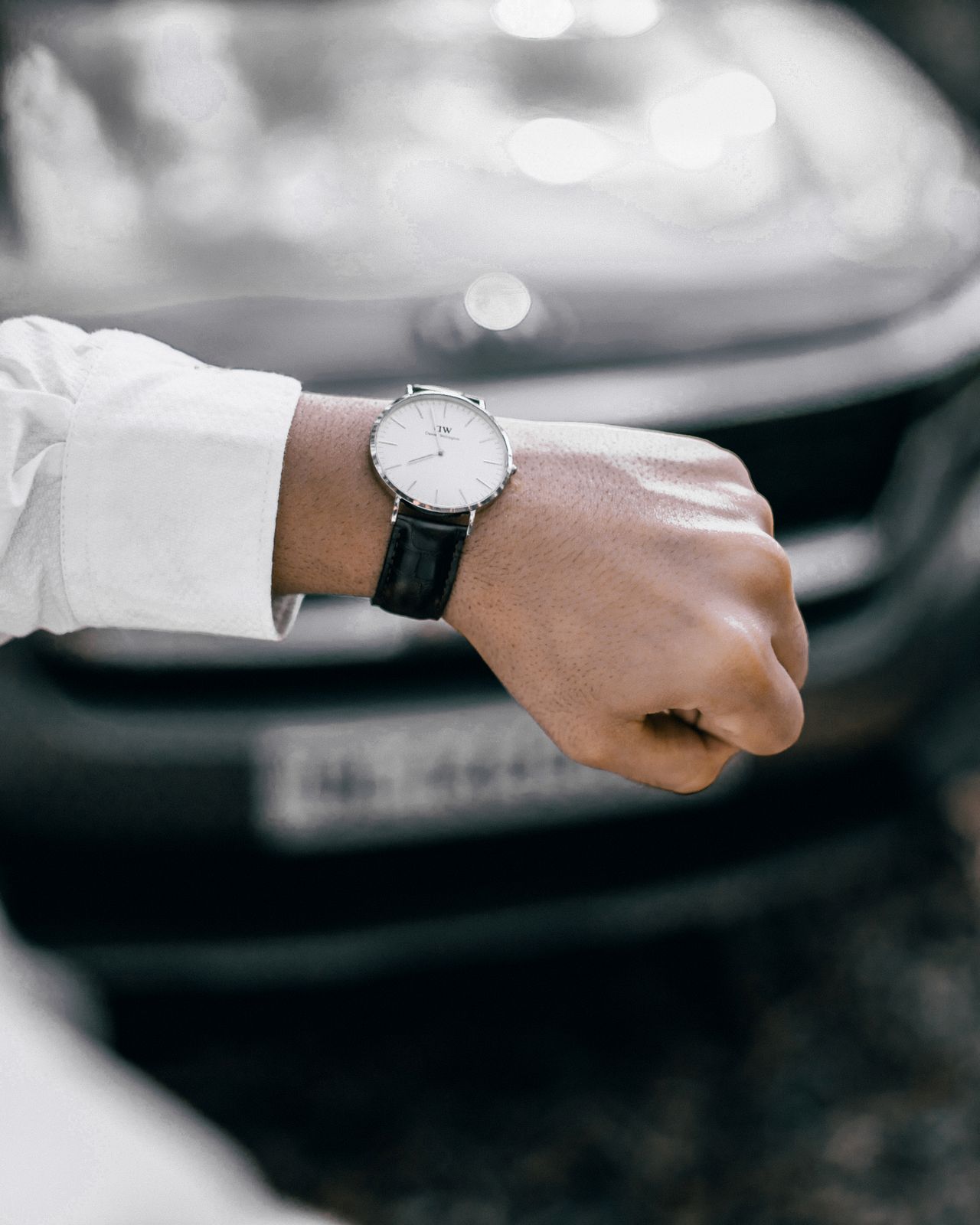 Muški Daniel Wellington sat s crnim kožnim remenom na ruci ispred automobila