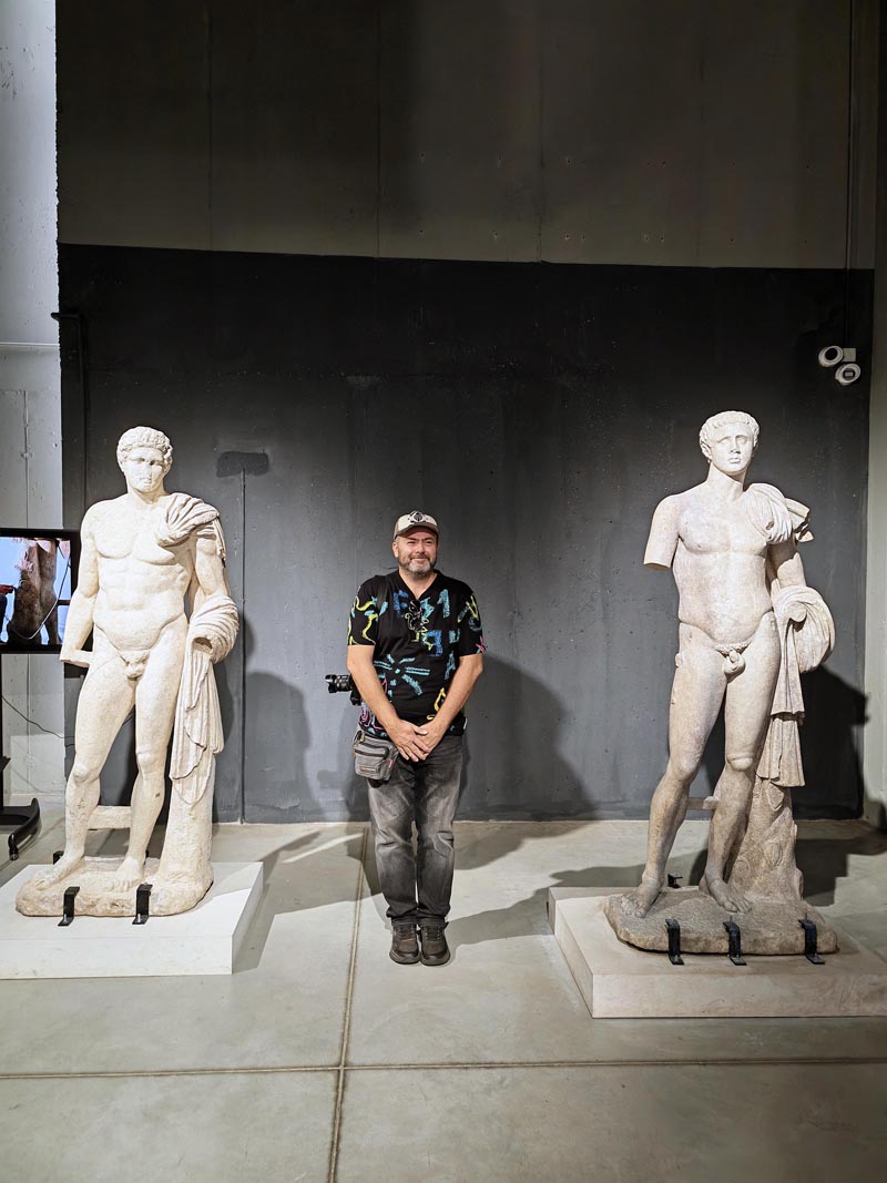 Nikola Zoko pozira između dvije antičke mramorne skulpture u Povijesnom muzeju u Petriču