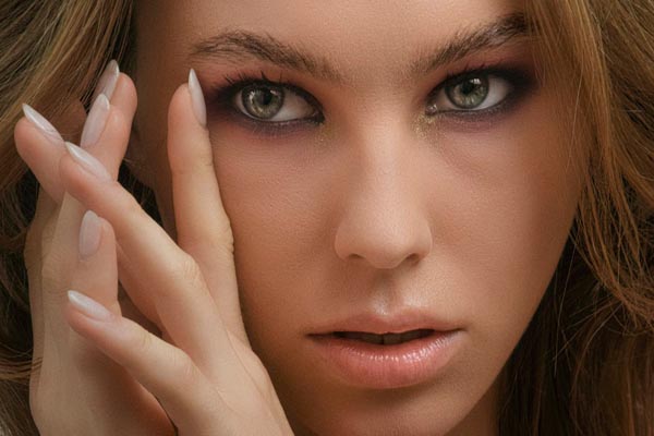 Krupni kadar lica žene sa smokey eye šminkom, zelenim očima i dugim mliječnobijelim noktima