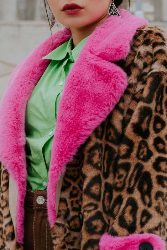 Krzneni kaput s leopard uzorkom i kričavo ružičastim ovratnikom preko zelene košulje i Prada naušnice