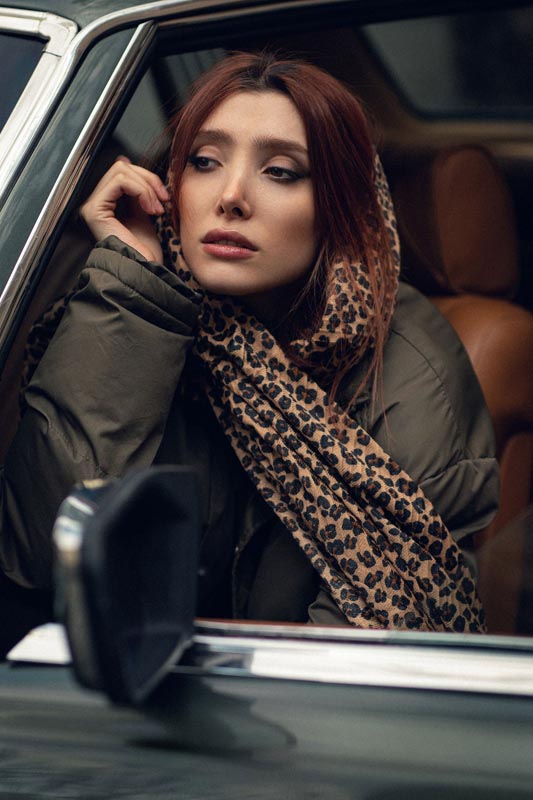 Crvenokosa žena s maramom leopard uzorka sjedi u automobilu i gleda kroz prozor