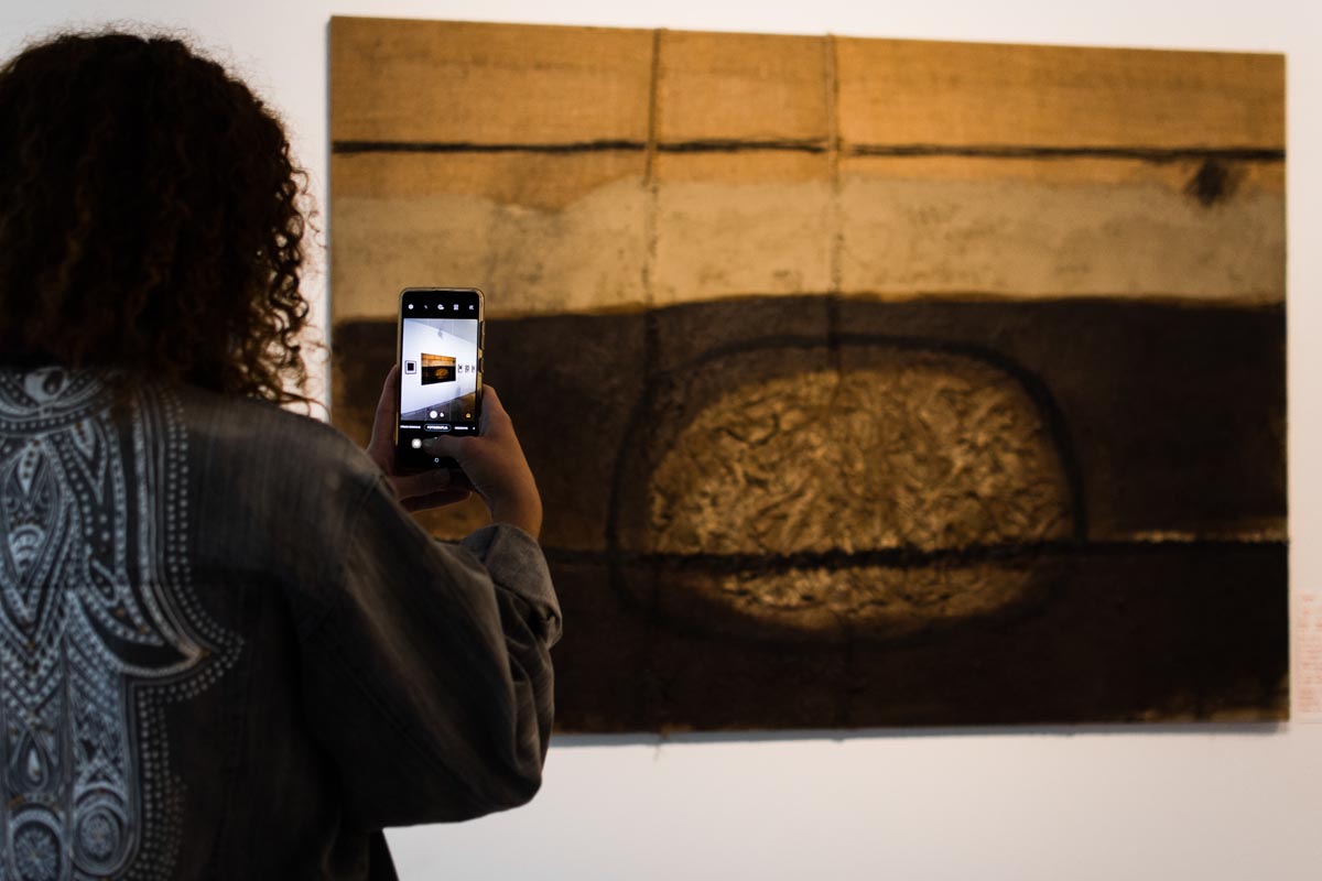 Djevojka pametnim telefonom fotografira apstraktnu sliku tamnih tonova na zidu galerije