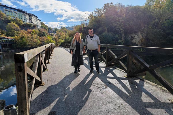 Nikola Zoko i Alma Premerl Zoko drže se za ruke na drvenom mostu na Bentbaši u Sarajevu s pogledom na Miljacku