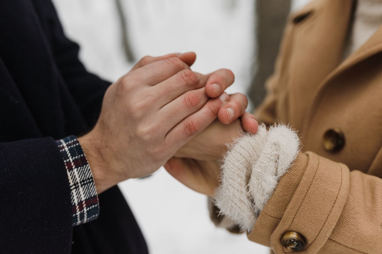 Muškarac nježno drži i grije ženske ruke u čupavim bijelim rukavicama tijekom zimske šetnje