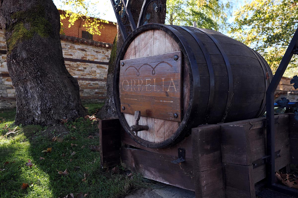 Velika drvena bačva s natpisom Orbelia ispred stare kamene zgrade vinarije okružene drvećem