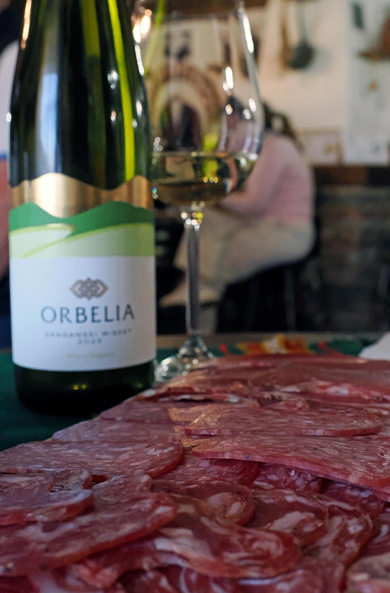 Boca bijelog vina Orbelia Sandanski Misket poslužena uz čašu vina i bogatu platu narezane trajne salame