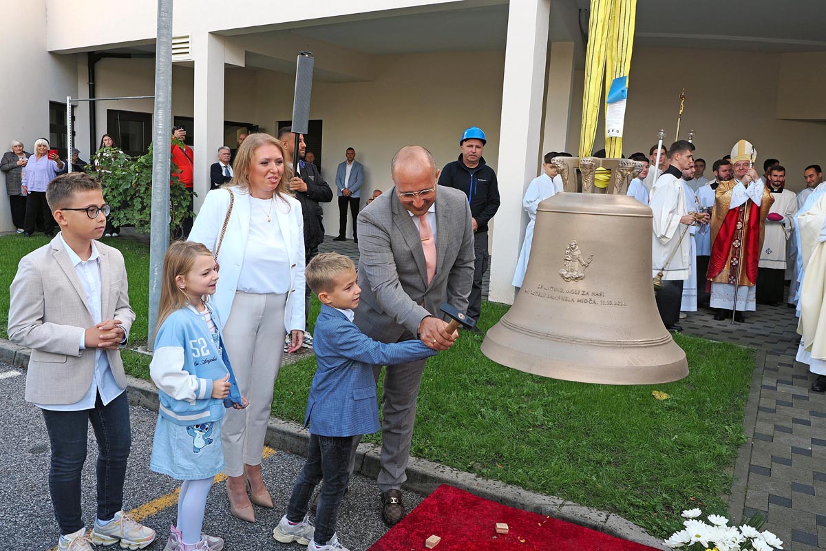 Otac i sin Mioč čekićem simbolično udaraju u novo crkveno zvono ispred župe svetog Ivana XXIII.