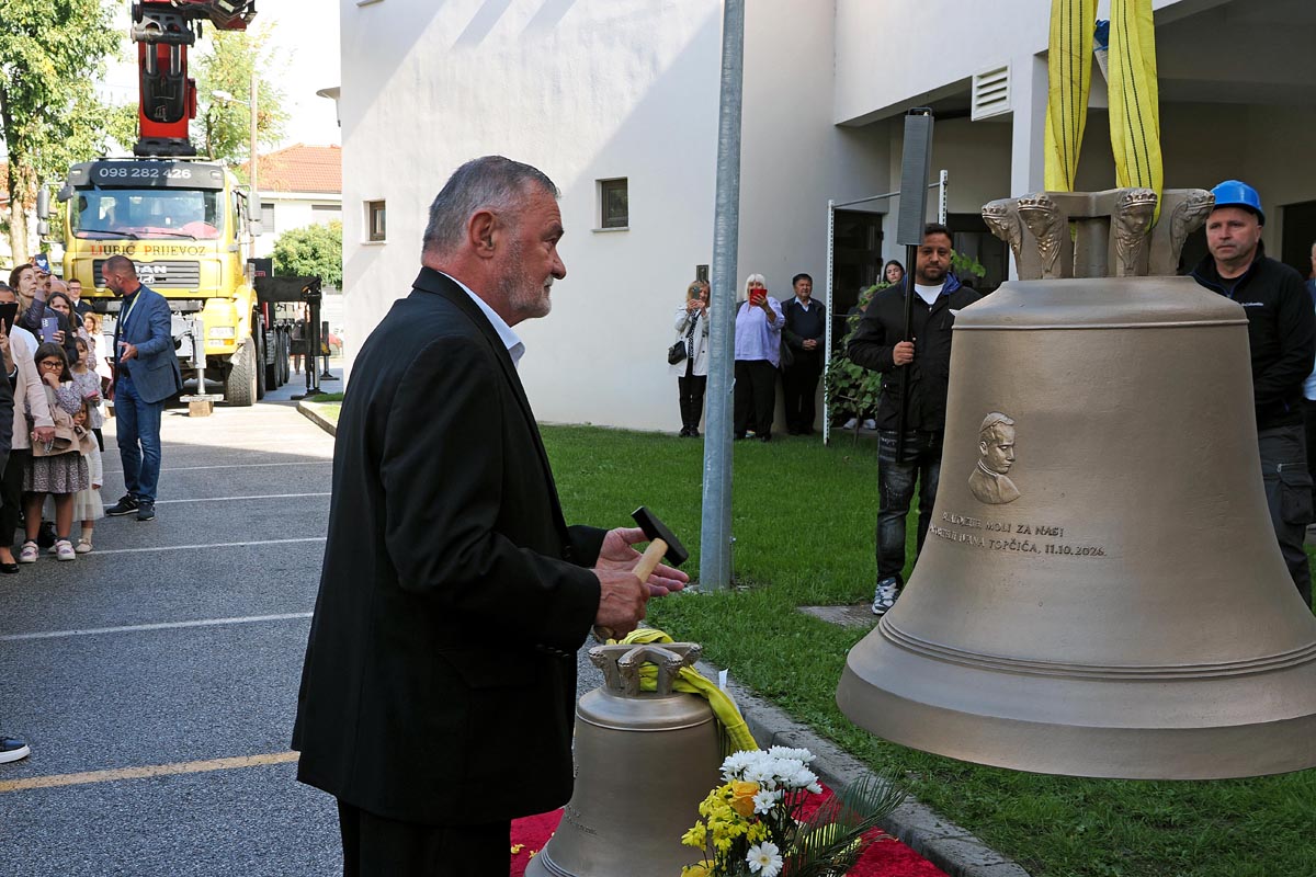 Ivan Topčić s čekićem u ruci stoji ispred novog crkvenog zvona s reljefom u dvorištu župe sv. Ivana XXIII.